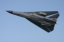 Underside view of pale gray aircraft with wings fully swept, making it appear triangular