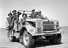 A military vehicle in the desert with five soldiers aboard.