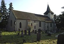 Photograph of a church with roughcast walls and square belltower. A number of gravestones are visible in the foreground
