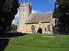 A church seen between two yew trees with a tower on the left and the body of the church, with an arched porch, stretching to the right
