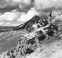 Camouflaged Sherman headed up a steep hill with troopers attending to the tracks.