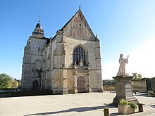 Photographie d'une église et d'une statue de sainte voilée sur socle au premier plan à droite