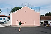 Photographie d’un homme jouant à la pala sur le mur d’un fronton rose.