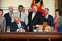Members of the General Assembly, Attorney General Anthony Brown, and advocates stand around Governor Wes Moore and House Speaker Adrienne Jones as he signs the Child Victims Act.