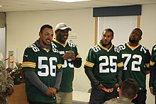 Grant standing with other Packers alumni, who are wearing their jerseys, talking with soldiers.