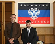 Two serious-looking men in front of a Donetsk People's Republic flag