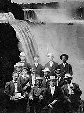 A dozen African American men seated with Niagara Falls in the background