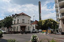 Photographie en couleur de bâtiment au second plan, surplombés par une grande cheminée.