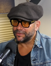 A man who is wearing glasses is speaking on a microphone