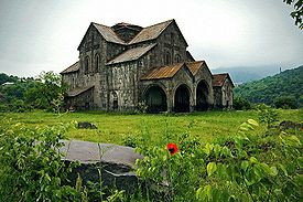 Ancient stone church with many gables sits in a grassy area that is surround by vegetation.