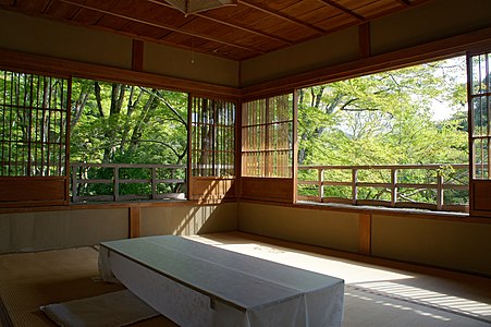 room with sliding screens at about 50 cm height, looking out on the upper reaches of sunlit trees. The screens have a low wooden panel, and a high lattice which appears to be open but is actually glass-filled.