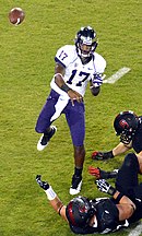 An African-American man wearing a white football jersey emblazoned with number 17 and purple pants throws a pass; the hands of various defenders are visible.