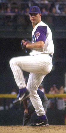 A man in a white baseball uniform and purple cap