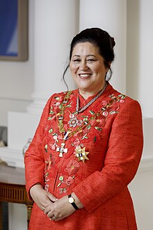 A smiling woman wearing a red dress with ribbons and badges