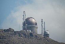 An observatory on a mountain, against a blue sky and a white cloud.