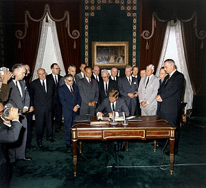 נשיא ארצות הברית ג'ון פ. קנדי מאשרר את האמנה למניעת ניסויים גרעיניים באטמוספירה, בחלל החיצון, ותחת פני המים בחתימת ידו בבית הלבן, ב-7 באוקטובר 1963, בנוכחות סגן הנשיא לינדון ג'ונסון, מזכיר המדינה דין ראסק, ומספר סנאטורים.