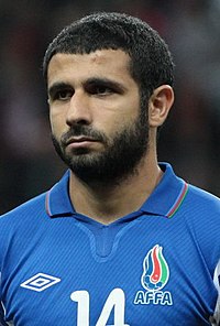 A bearded man in a blue top sits behind a desk at a press conference