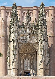 Portail d'entrée d'une église de brique surmonté d'un baldaquin de pierre élevé et très ouvragé par de nombreuses sculptures.