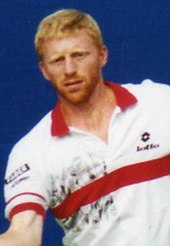 A blonde, bearded man in a white and red polo shirt swings his arm during a tennis rally