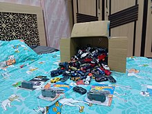A cardboard box full of Hot Wheels cars spilling into a blue bed