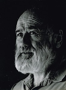 Photographic portrait in black and white. John Bevan Ford is an older man in this photo, with a grey beard and expressive face. He looks off to the side.