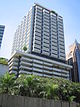 Box-like building with rectangular cross section. The lower floors are a visible parking garage, while the upper floors have a grey and white facade with protruding windows and a rooftop terrace.