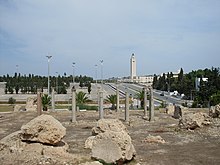 Vue générale d'un édifice ruiné avec des colonnes et avec au fond de l'image une mosquée