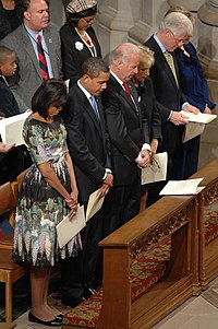 From left to right: the Obamas and two other couples stand with their heads bowed in a pew