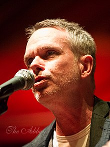 Rick Price singing into a microphone with a dark red background