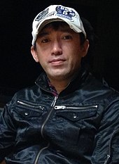 A photograph of a Japanese man wearing a baseball cap.