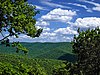 View from a lookout of green tree-covered mountains under a blue sky with white clouds