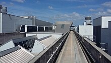 An empty concrete train guideway on the roof of an airport terminal building, with a train on the left traveling on a seperate, parallel guideway.