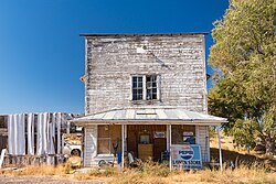 Abandoned 2-story wooden storefront. A closed sign is nailed to the door, and the porch is covered in junk.