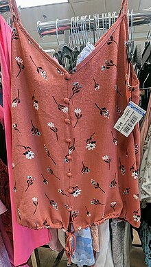 A floral summer top/blouse on hanger inside of a local thrift store, with price tags listed at $4.29.