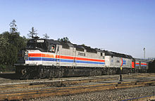 A passenger train led by two diesel locomotives. The first locomotive has a black roof, light gray sides, and red and blue horizontal stripes separated by a thin white stripe. The second locomotive has a black roof, gray sides, and a red-and-blue Amtrak logo on the side.