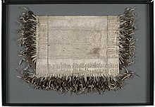 A weathered piece of parchment 20 inches long and 30 1/2 inches wide with faded Latin text in the centre and a 100 signatures around the sides with corresponding wax seals attached.