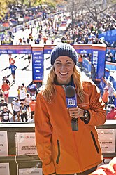 A women holds a microphone in front of a finish line