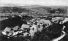 Photographie vue de loin d'un sanctuaire shinto. Plusieurs sont présents sur une colline, avec au loin une ville.