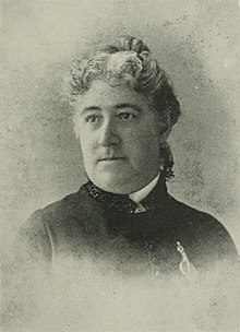 B&W portrait photo of a woman with her gray hair in an up-do, wearing a dark jacket.