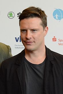 close-up of Florian Panzner wearing dark t-shirt and blazer, smiling left of camera