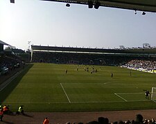 A panorama of a semi-full football stadium with green seats on a sunny day.