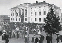 People gathered in front of the new city hall, which is white with two stories and stately features