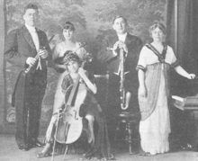 The Smith-Spring-Holmes Orchestral Quintet, from a 1915 publication. Five white people, two men and three women, in formal attire; the men are holding a clarinet and saxophone; the women are shown with a violin, cello, and piano.