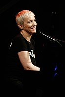 Annie Lennox performing on a piano while smiling