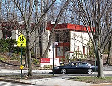 Modern-style white brick building with red trim set into a wooded hillside. The sign in front reads "Society for Ethical Culture"