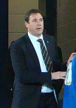 The head and torso of a man in his 30s or 40s, wearing a shirt, tie and blazer.