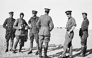 Informal portrait of six men standing in the desert, wearing military uniforms and flying gear