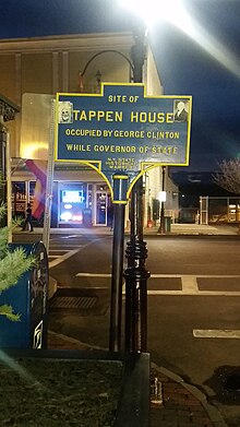 a picture of the marker at night, there are stickers on the marker, one showing the face of NY State Governor Clinton, the other of the rock musician