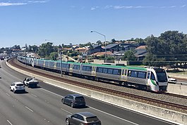 Six car electric multiple unit train running on tracks within the median strip of a freeway