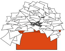 Two eyes peeking out from under a pile of papers atop a desk